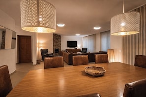 Uma sala de estar moderna com lareira, sala de jantar com mesa e cadeiras de madeira, e área de estar com sofás e televisão.