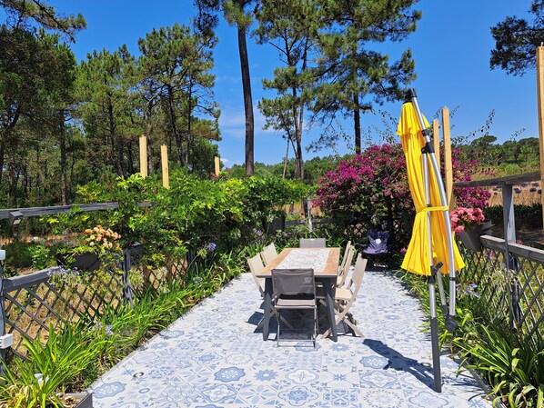 An outdoor patio with a table and chairs, surrounded by lush greenery and flowering plants.