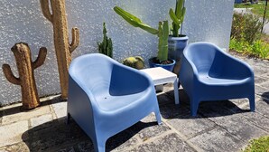 A patio with two blue plastic chairs, a small white table, and a potted cactus plant. - Villa Leglise Chafe plage d' Amorosa - Viana - pets welcome. (Chafé)