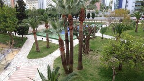 A landscaped area with palm trees, a paved walkway, and a view of a parking lot with cars. - FANTASTIC LOFT APARTMENT ON THE BEACH WITH ALL SERVICES (WIFI, A / C) (Alicante)