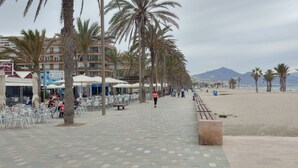 A seaside promenade with outdoor seating, palm trees, and a beach in the background. - FANTASTIC LOFT APARTMENT ON THE BEACH WITH ALL SERVICES (WIFI, A / C) (Alicante)