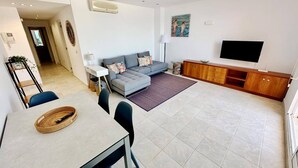 Una sala de estar moderna con un sofá gris, una mesa de comedor con sillas, un televisor y un aparador de madera.