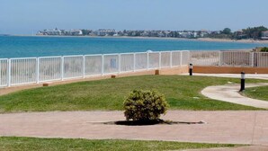 Un paseo marítimo con valla blanca, un arbusto pequeño y una vista despejada de la playa y el océano.