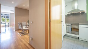 A modern kitchen with stainless steel appliances, a dining area with a glass table and chairs, and a view of the outdoors through a large window. - INNER CITY CENTER ON PASEO DE GRACIA, luxurious & spacious, family & friends    (Barcelona)