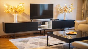 A modern living room with a flat-screen TV on a black entertainment unit, two white vases with golden decorative elements, a beige sofa, and a patterned rug. - INNER CITY CENTER ON PASEO DE GRACIA, luxurious & spacious, family & friends    (Barcelona)