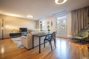 A modern living room with a sofa, a dining table, a TV, and a green chair.
