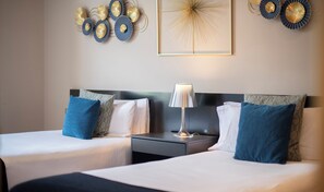 Une chambre d’hôtel avec deux lits, une table de chevet, une lampe et des œuvres d’art décoratives au mur.