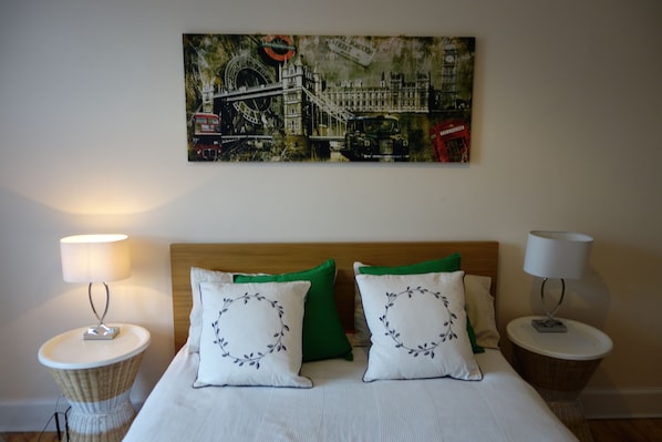 Un dormitorio con una cama, dos lámparas de noche, un cuadro colgado en la pared de un puente y dos almohadas con motivos florales.