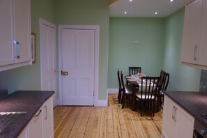 A kitchen with wooden flooring, white cabinets, and a dining table with chairs.