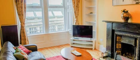 Una sala de estar con sofá, televisor, chimenea y ventana con cortinas.