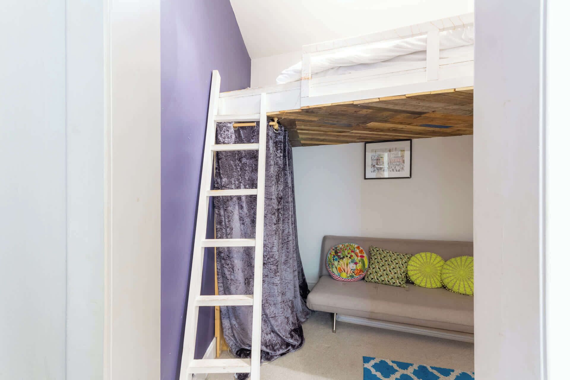 A room with a bunk bed, a ladder, a sofa with colorful cushions, and a framed picture on the wall.
