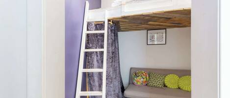 A room with a bunk bed, a ladder, a sofa with colorful cushions, and a framed picture on the wall.