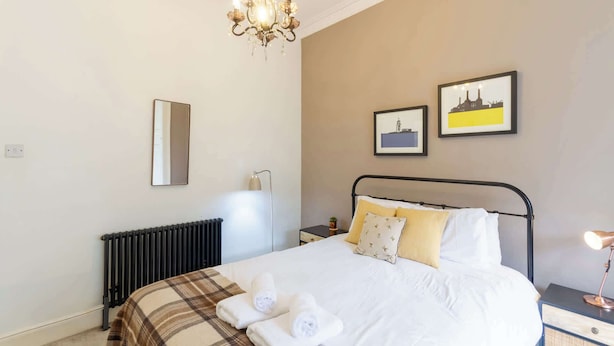 A bedroom with a bed, a radiator, a chandelier, a bedside lamp, and two framed pictures on the wall. - Beautifully Modernised New Town Home for 5 (Edinburgh)