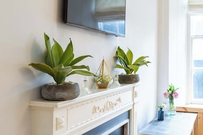 A fireplace with three potted plants, a decorative glass item, and a television mounted above.