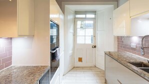 A kitchen with white cabinets, a granite countertop, a built-in oven, and a window above the door. - Beautifully Modernised New Town Home for 5 (Edinburgh)