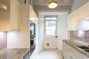 A kitchen with white cabinets, a granite countertop, a built-in oven, and a window above the door. - Beautifully Modernised New Town Home for 5 (Edinburgh)