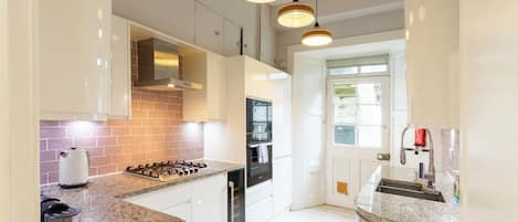Una cocina moderna con armarios blancos, estufa a gas, horno empotrado e iluminación colgante.