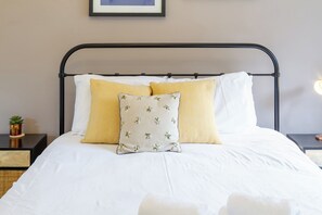 A bed with white bedding and two pillows, one with a geometric pattern and the other with a floral design. - Beautifully Modernised New Town Home for 5 (Edinburgh)
