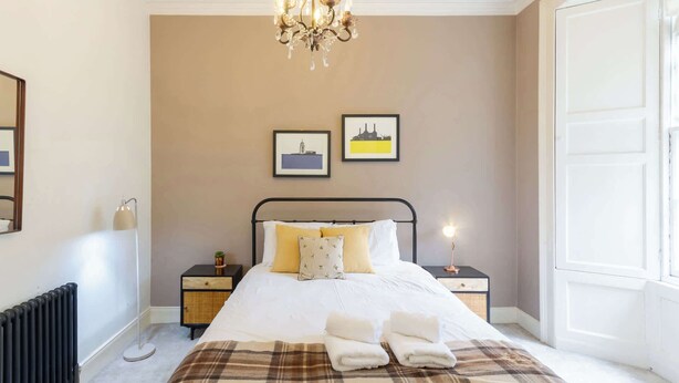 A bedroom with a bed, bedside tables, a radiator, a chandelier, and two framed pictures on the wall. - Beautifully Modernised New Town Home for 5 (Edinburgh)