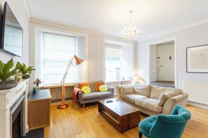 En stue med sofa, lænestole, sofabord, gulvlampe og en lysekrone.