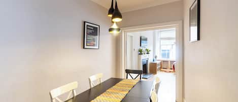 A dining area with a long table, chairs, and a patterned runner. There is a framed subway map on the wall and a door leading to another room.