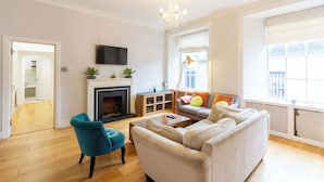 A living room with a fireplace, a sofa, a television, and a large window. - Beautifully Modernised New Town Home for 5 (Edinburgh)