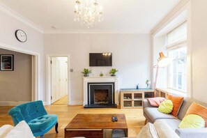 Una sala de estar con chimenea, un sofá, una mesa de centro, un sillón azul, una lámpara y un televisor en la pared.