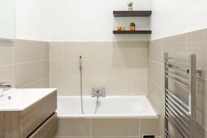 Un baño moderno con bañera, ducha, tocador con lavamanos y un perchero para toallas.