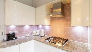 A kitchen with white cabinets, a gas stove, a toaster, and a coffee maker. - Beautifully Modernised New Town Home for 5 (Edinburgh)