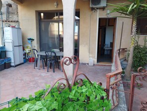 An outdoor patio with a table and chairs, a metal fence, and a palm tree.
