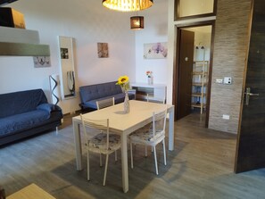 A modern living room with a dining table, chairs, a sofa, and a coffee table with a vase of flowers.