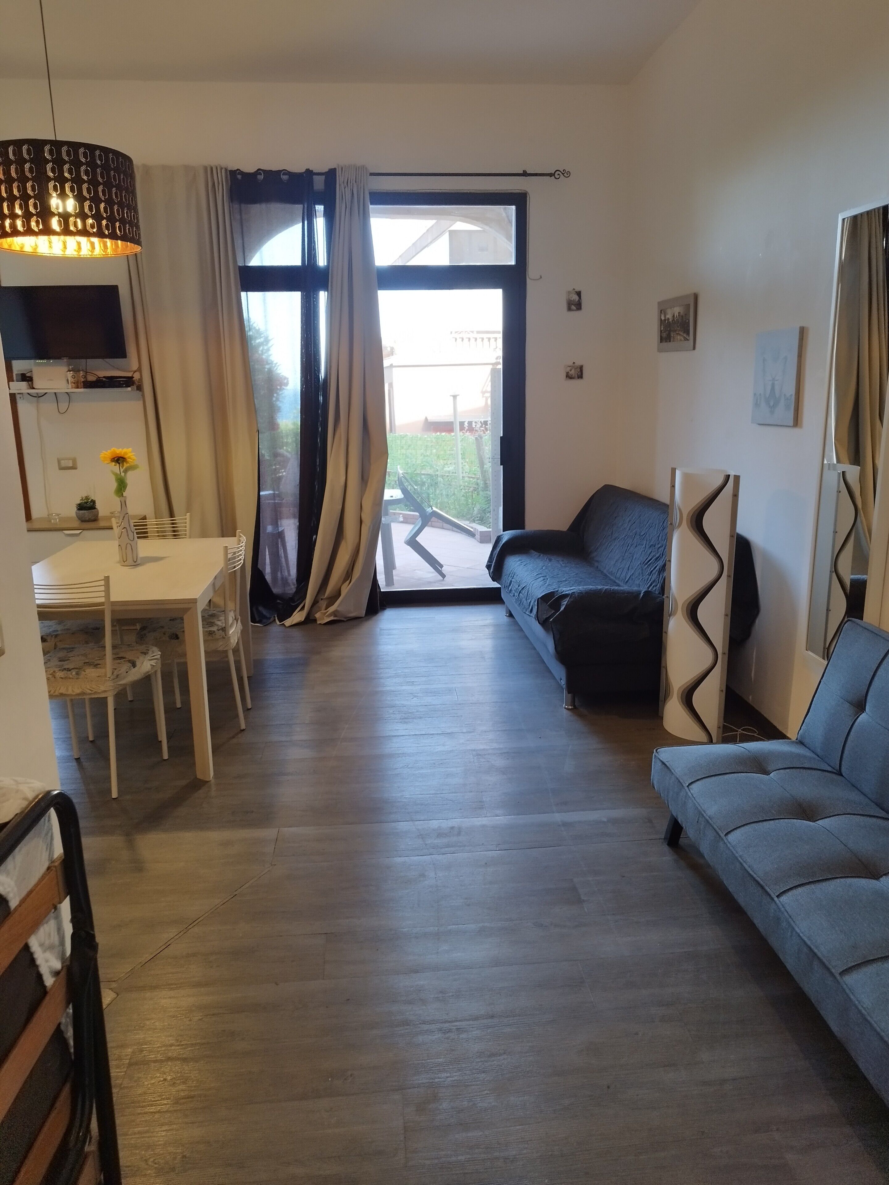 A living room with a sofa, a dining table with chairs, a TV, and a large window with curtains.