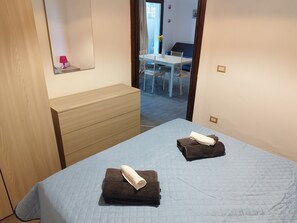 A bedroom with a bed, a dresser, and a view into a dining area.