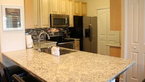 A kitchen with granite countertops, stainless steel appliances, wooden cabinets, and a tiled backsplash.