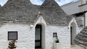 Ein traditionelles Steinhaus mit kegelförmigen Dächern, nummerierten Hauseingängen und Blumentöpfen.