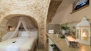 Ein Schlafzimmer mit Steinwänden, einem Himmelbett, einem Nachttisch mit Kerzen und einem Beistelltisch mit einer Laterne.