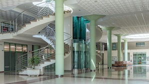Een ruime lobby met een centraal spiraaltrap, grote zuilen en een glazen liftput.