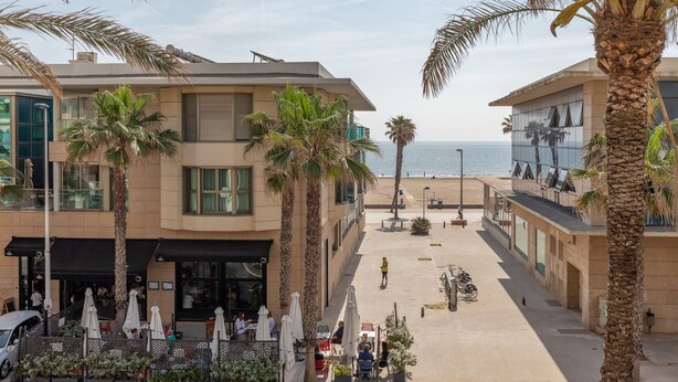 Een strandhotel met buitenzitplaatsen, palmbomen en uitzicht op zee.