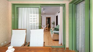 Een houten tafel met een lantaarn, een groene schuifdeur en uitzicht op een woonkamer met een bank en een eettafel.