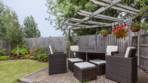 Eine Terrasse im Freien mit Korbmöbeln, einem Tisch und hängenden Blumenkörben.