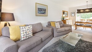 Ein Wohnzimmer mit zwei grauen Sofas, einem Glastisch und einem Essbereich mit Holzmöbeln.