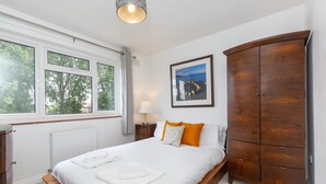 Ein Schlafzimmer mit einem großen Bett, einem Holzschrank, einem gerahmten Bild an der Wand und einem Fenster mit Vorhängen.
