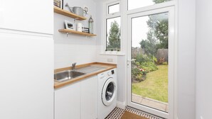 Eine kleine Küche mit integriertem Waschmaschinenanschluss, einer Holz Arbeitsplatte und einem Fenster mit Blick auf einen Garten.