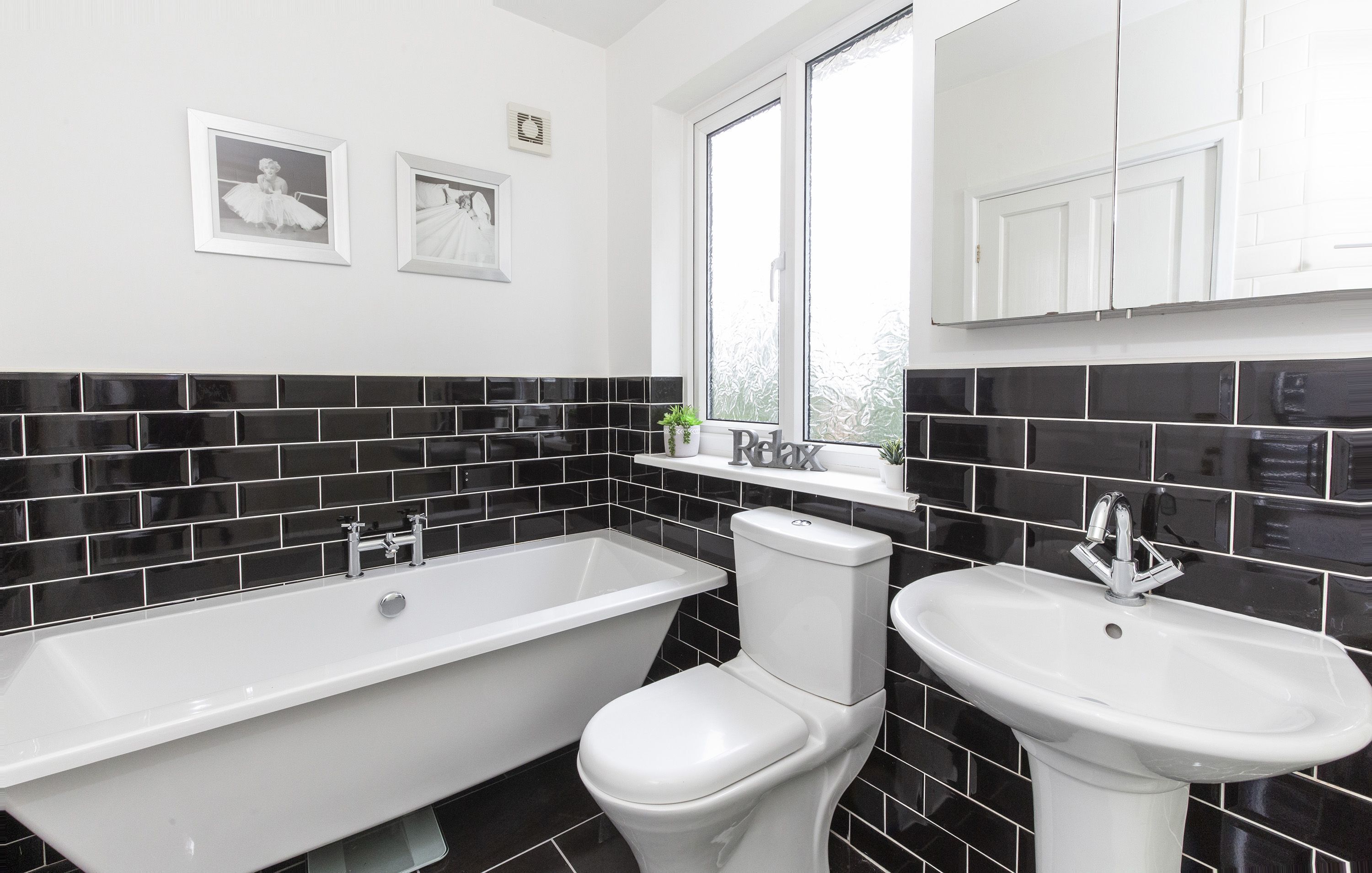 Un bagno moderno con vasca, water e lavabo, caratterizzato da piastrelle bianche e nere e quadri appesi alle pareti.