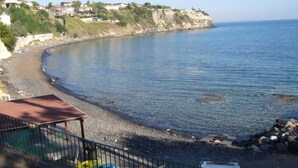 A coastal area with a rocky beach, a small structure with a roof, and kayaks.