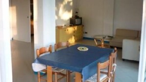 A small dining area with a table and chairs, a kitchenette in the background, and a sofa.