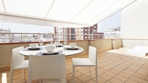 Una terrazza sul tetto con un tavolo rotondo apparecchiato per mangiare, sedie bianche e vista sulla città.