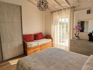 A bedroom with a large bed, a wooden bench with red pillows, a dresser, a mirror, and a hanging light fixture.
