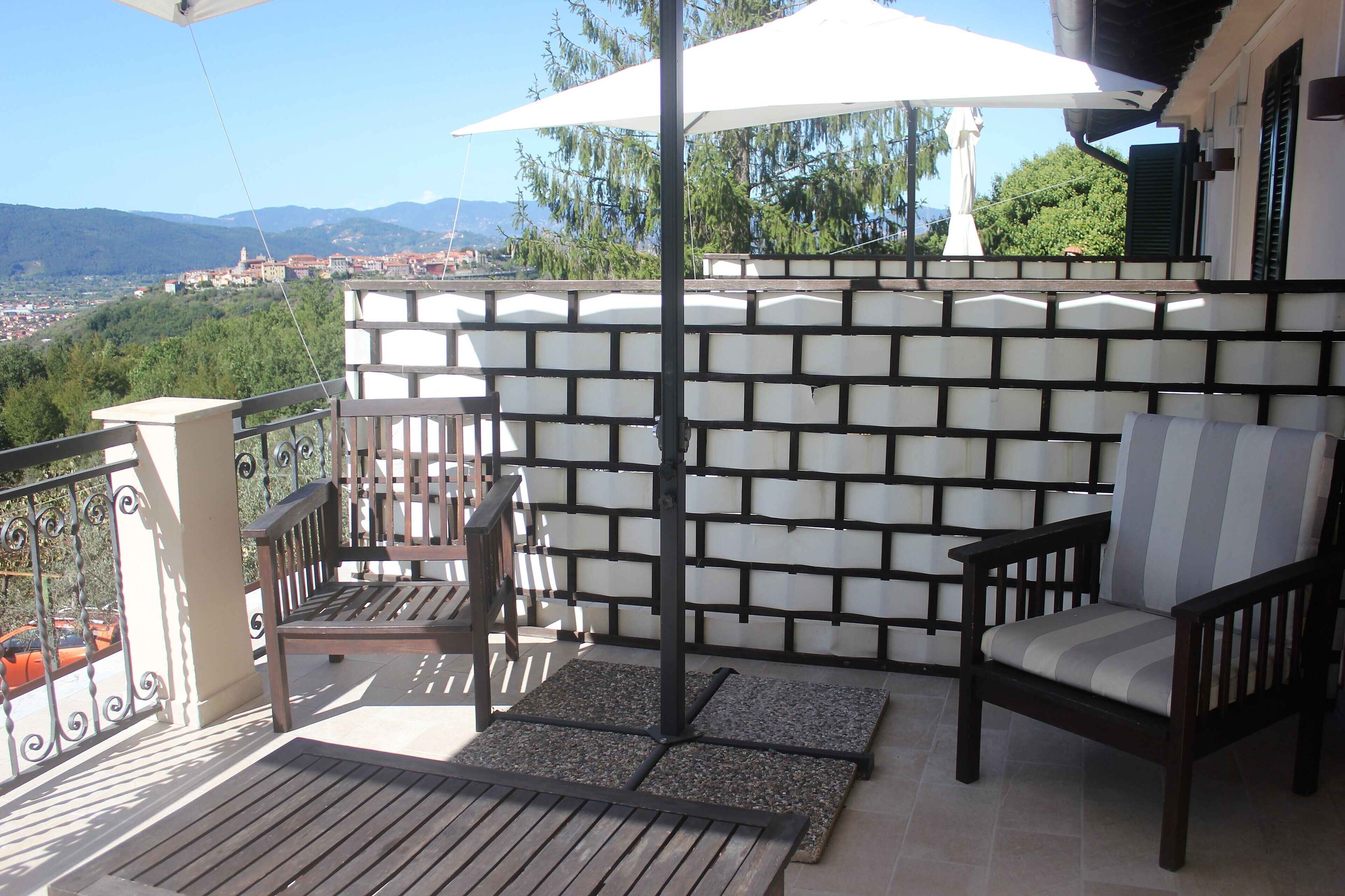 Un balcón con un banco de madera, una silla con cojín y una sombrilla blanca.