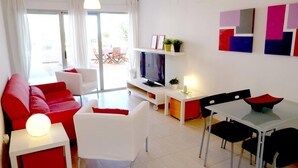 A modern living room with a red sofa, white armchairs, a TV, and a dining area with a table and chairs. - Tierra de Mar 60 by homeprive (Denia)